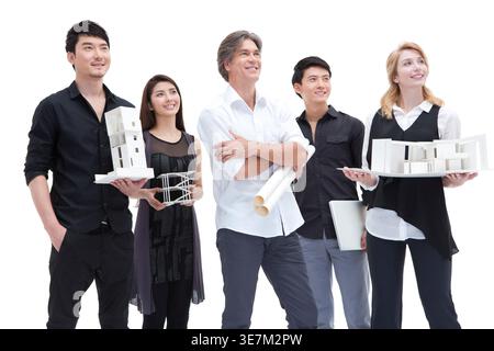 Chinese and caucasian architects holding architectural model looking away while standing against white background in studio Stock Photo