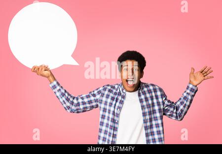 Surprised Black man pointing finger up holding blank speech bubble standing against pink background in studio Stock Photo