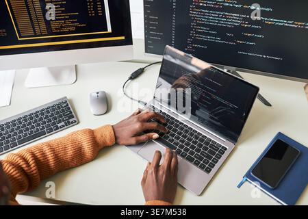 Cropped image of Black male programmer working on laptop while sitting at table in office Stock Photo