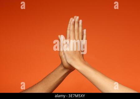 Black couple doing high five together against orange background in studio Stock Photo