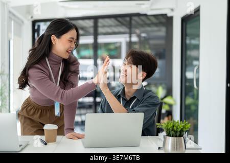 Asian male and female office workers giving high five to each other in office Stock Photo
