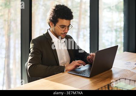 Mixed-race businessman looking at laptop screen working over new project while sitting at table in office Stock Photo