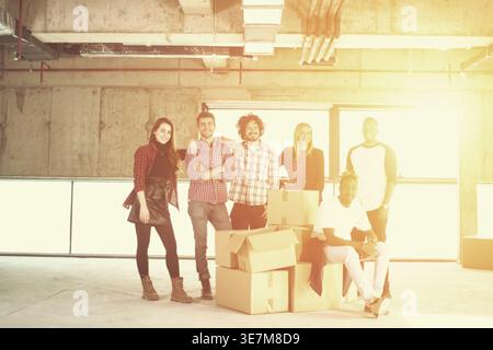 Group of diverse business people standing together with Black man sitting on cardboard boxes in empty unfinished office building Stock Photo