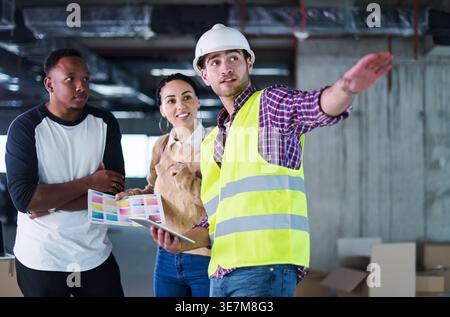 Middle Eastern woman and Black man standing and talking to caucasian male architect explaining plans inside the building Stock Photo