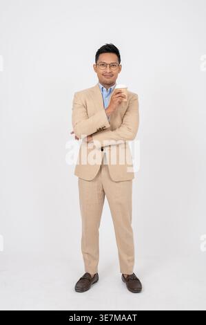 Smiling Asian businessman wearing eyeglasses leaning elbow on arm holding coffee cup standing against white background in studio Stock Photo