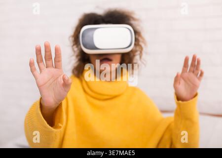 Black woman wearing VR headset experiencing virtual reality standing indoors Stock Photo
