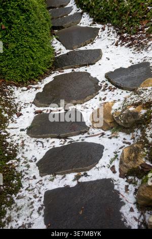 Dark stone stepping stones on a garden path covered with a light dusting of white snow during January in winter Stock Photo