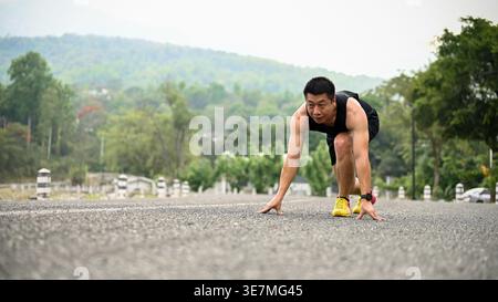 Asian man in sportswear leaning forward with hands on ground preparing to run outdoors Stock Photo