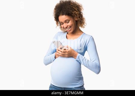 Smiling mixed race pregnant woman standing and using smartphone in white background studio Stock Photo