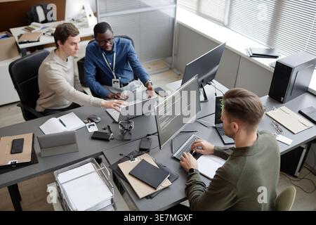High angle view of diverse group of male IT specialists working together sitting at desk with laptop and computers in office Stock Photo