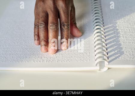 Hand of Black man reading braille at table at home Stock Photo