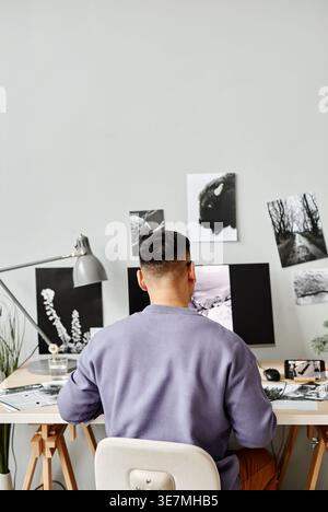 Asian male photo editor editing photos sitting at table with computer in office Stock Photo