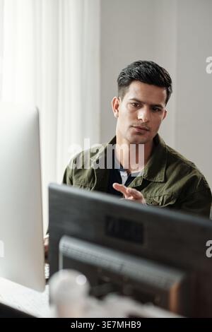 Indian male programmer sitting at desk in front of computer in office Stock Photo