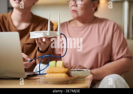 Asian grandmother wearing eyeglasses learning how to setup wifi router with her grandson while sitting on sofa at home Stock Photo