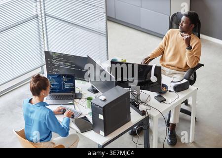 Black male programmer looking away sitting at table near caucasian female colleague typing on computer in office Stock Photo