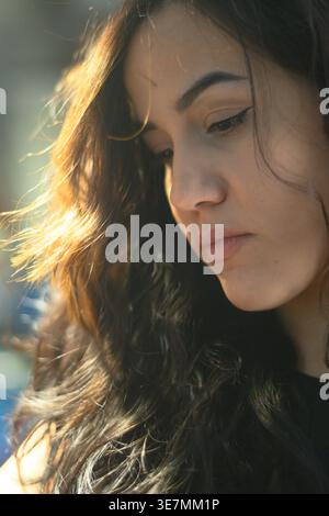 Hispanic female mechanic with wavy long hair looking down standing in auto repair shop Stock Photo