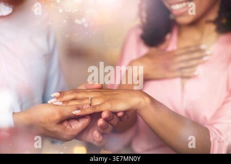 Cropped image of Black man putting engagement ring to girlfriend after proposing indoors Stock Photo