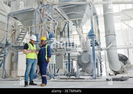 Mixed-race female and caucasian male engineers using tablet together standing in factory Stock Photo