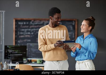 Black male and caucasian female programmers using tablet looking at each other while standing in office Stock Photo
