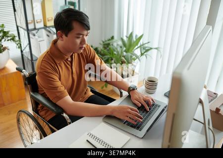Asian male with disability working on laptop sitting at desk in office Stock Photo