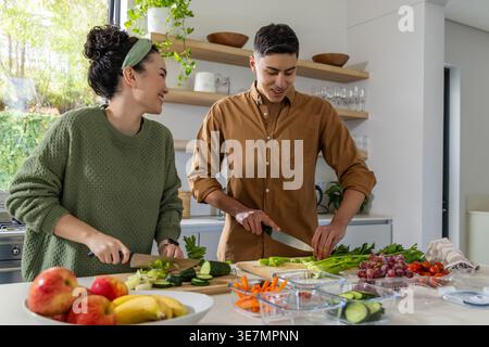 Diverse couple chopping and arranging fresh produce on kitchen island with cutting boards Stock Photo