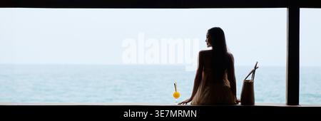 Asian woman wearing summer dress looking over shoulder sitting in waterfront restaurant during daytime Stock Photo