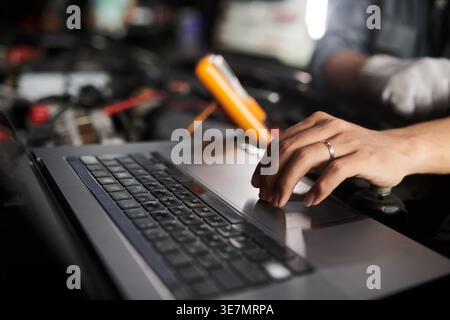 Asian male mechanic checking car engine using multimeter and laptop while standing in auto repair shop Stock Photo