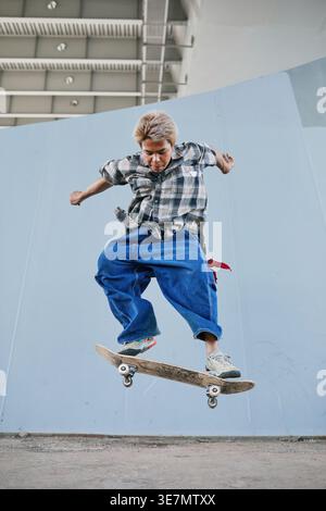 Asian male skateboarder performing tricks on ramp in skate park during daytime Stock Photo