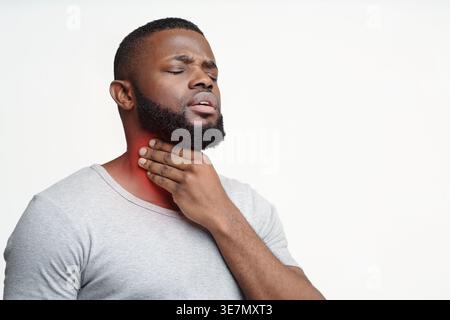 Black man suffering from sore throat touching neck while standing against white background in studio Stock Photo