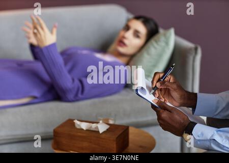 Cropped image of Black male psychologist taking notes during therapy session with female client in office clinic Stock Photo