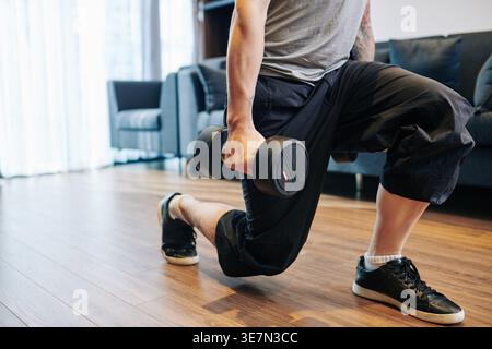 Mixed-race man doing lunges with dumbbells in apartment Stock Photo