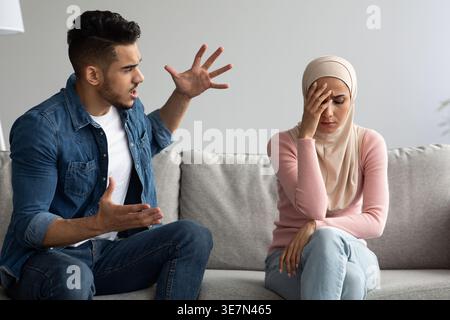 Middle Eastern man yelling at his irritated girlfriend while sitting on sofa at home Stock Photo