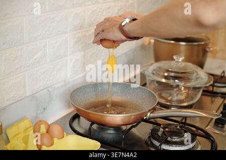 Cropped image of Asian male hands cracking egg on pan while cooking in kitchen at home Stock Photo