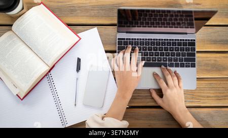 Hispanic female college student studying and using laptop sitting at table with pen, book and smartphone in university campus Stock Photo