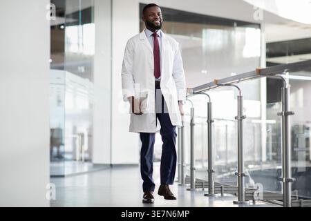 Bearded Black male scientist in white robe holding tablet walks into research center Stock Photo