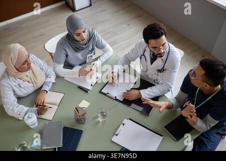 Diverse group of doctors having meeting while sitting together at table with documents in office clinic Stock Photo