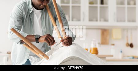 Black man using allen wrench assembling chair standing in kitchen at home Stock Photo