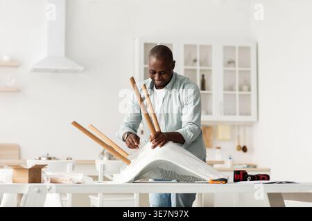 Black man assembling chair standing in kitchen at home Stock Photo