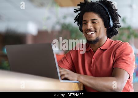Black male with afro with headphones using laptop sitting at table in cafe Stock Photo