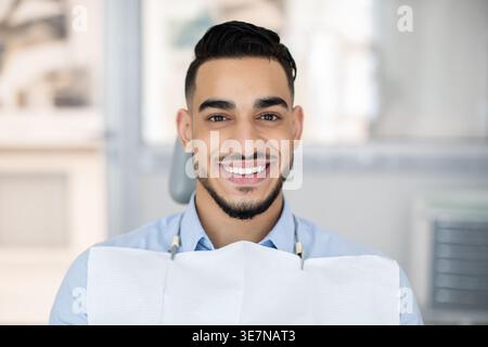 Portrait Of Handsome Young Arab Man Sitting In Chair In Dental Clinic, Smiling Middle Eastern Guy Waiting For Check Up And Medical Treatment In Modern Stock Photo