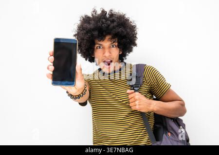 Surprised African American man with backpack showing smartphone standing against white wall Stock Photo
