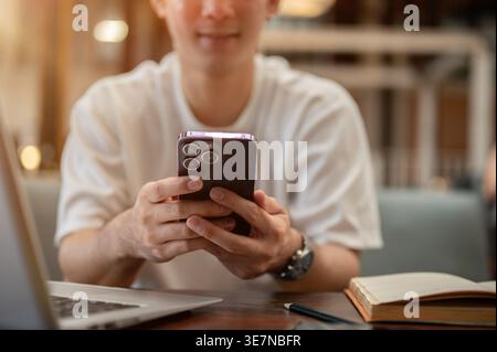 Cropped image of Thai man using smartphone sitting at table in cafe Stock Photo