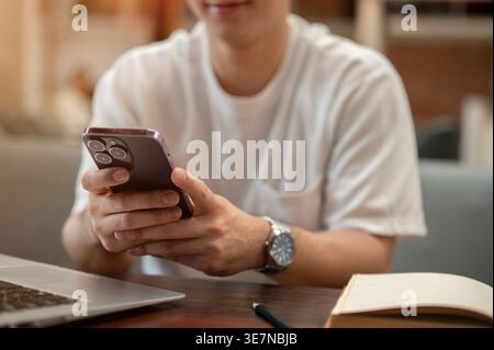 Cropped image of Thai man using smartphone sitting at table in cafe Stock Photo