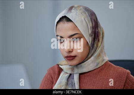 Mixed-race Muslim female wearing headscarf looking at laptop screen working while sitting in office Stock Photo