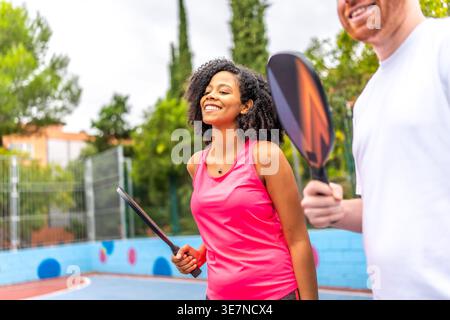 Smiling diverse group of friends playing pickleball together in outdoor court during daytime Stock Photo