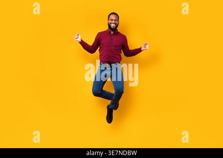 Black man jumping against yellow background in studio Stock Photo