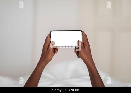 Hands of Black man using smartphone while lying on bed at home Stock Photo