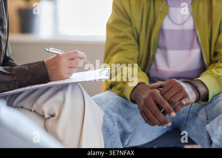 Cropped image of Black man sitting next to psychotherapist taking notes during therapy session in clinic Stock Photo