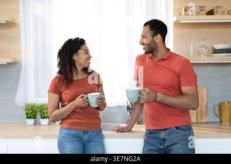 Black couple talking and drinking coffee together while standing in kitchen at home Stock Photo
