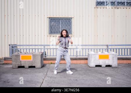 Asian woman in shirt and jeans dancing in city street during daytime Stock Photo